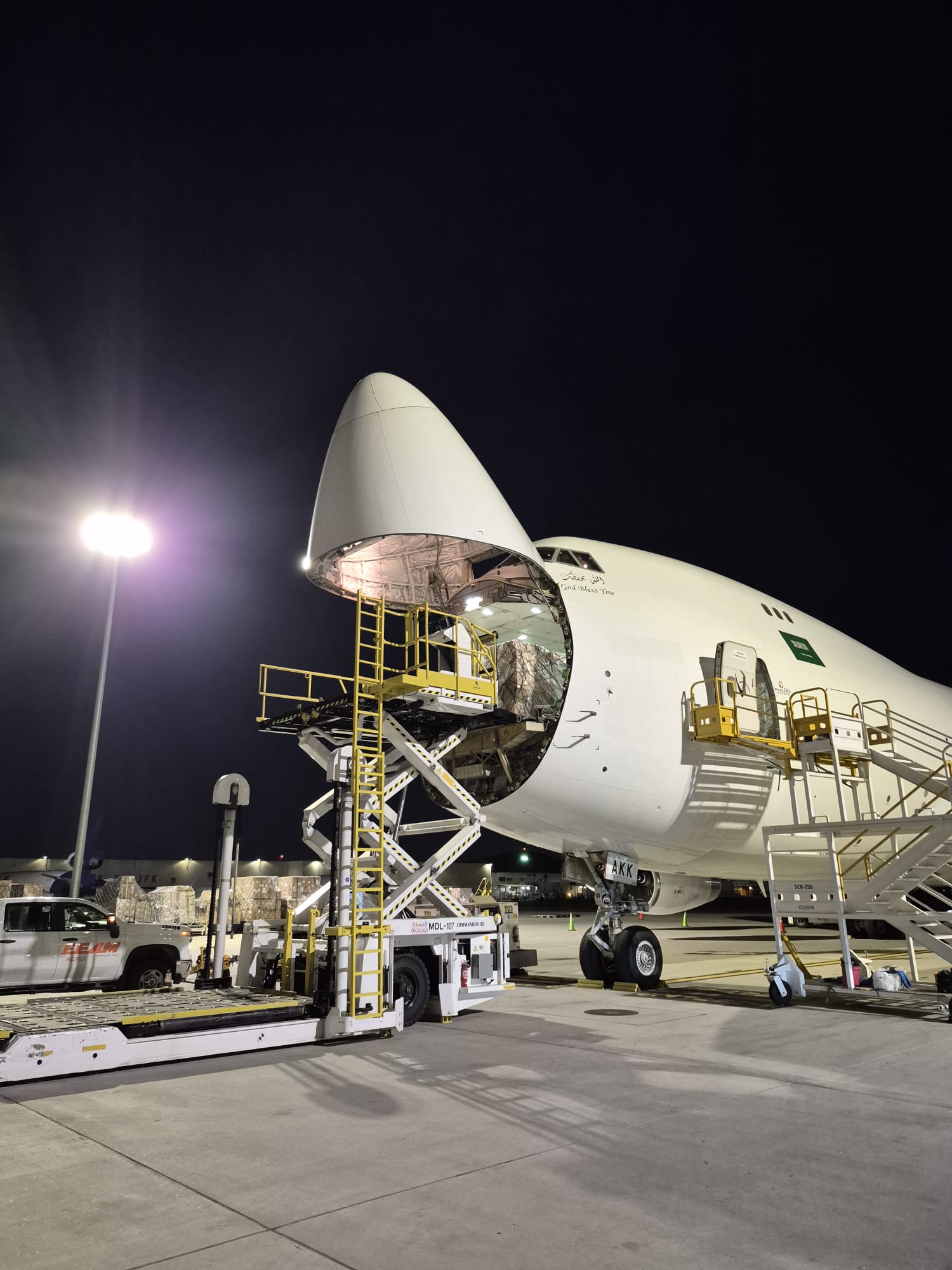 Boeing 747 freighter with open nose door being loaded at night under apron floodlights