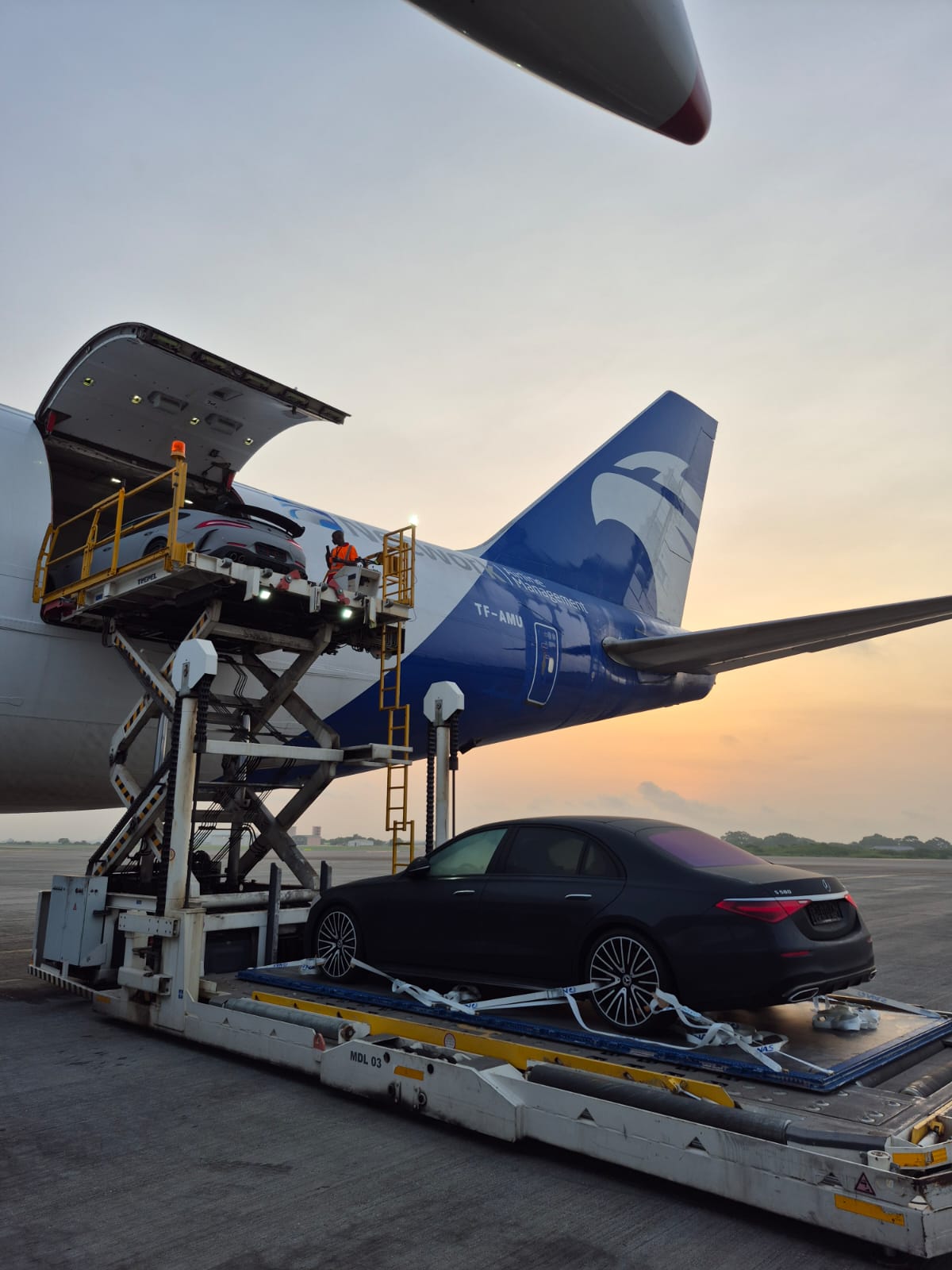 Luxury car on a cargo loader beside a widebody freighter at sunset